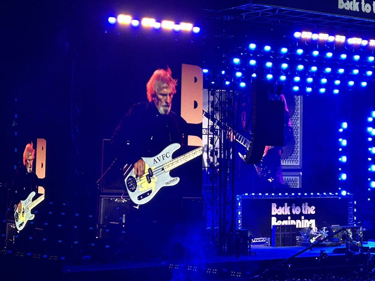 Geezer Butler, en las pantallas de Villa Park, toca un bajo con el escudo del Aston Villa durante el concierto Back to the Beginning de 2025